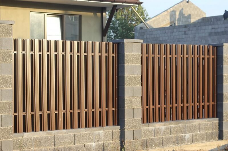 Забор из светло-коричневого металлического штакетника с каменными столбами